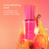 image of amika:aura hair + body mist in front of an orange and pink background with pink grapefruit, juicy apricot and warm vanilla around the bottle. text: "aura-activating scent" "an uplifting burst of pink grapefruit, juicy apricot + warm vanilla" 