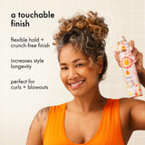 Woman holding a bottle of amika fluxus touchable hairspray with text about its features.