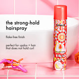 Amika headstrong hairspray bottle with text on a pink tiled background