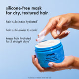 Amika Hydro Rush mask jar with a hand applying the product against a light blue background