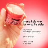 Amika strong-hold wax jar held by a hand with product description text on a pink background