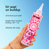 Pink bottle of amika product held by a hand against a blue background