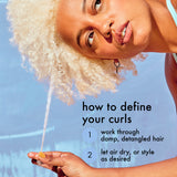 Woman with blonde curly hair holding a strand of hair against a blue sky.