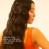 Woman with long, wavy hair wearing an orange top against a beige background