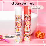 Two hair spray bottles with colorful designs on a pink tiled background.