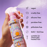 Hand holding a 'amika' spray bottle with product features listed on a purple background