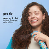Woman with curly hair using a hair product against a blue background