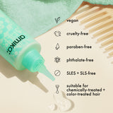 a bottle of amika the kure multi-task treatment lies on a white surface with a bit of the treatment spilling out. Text outlines details about this product: vegan, cruelty-free, paraben-free, phthalate-free, SLES  SLS-free, suitable for chemically treated + color-treated hair. 