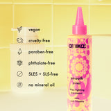 Amika smooth over frizz-fighting treatment bottle with product features listed on a yellow tiled background
