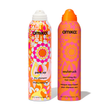 Two full-size amika aerosol products: Perk Up Dry Shampoo on the left with a white cap and colorful orange, pink, and yellow pattern; Soulstruck Nourishing Dry Hair Mask on the right with an orange cap and warm pink-orange illustrated design.