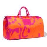 image of amika's duffle bag - turned slightly to the side - an orange and pink bag with a pink logo plate and pink handles. the bag sits on a white background. 